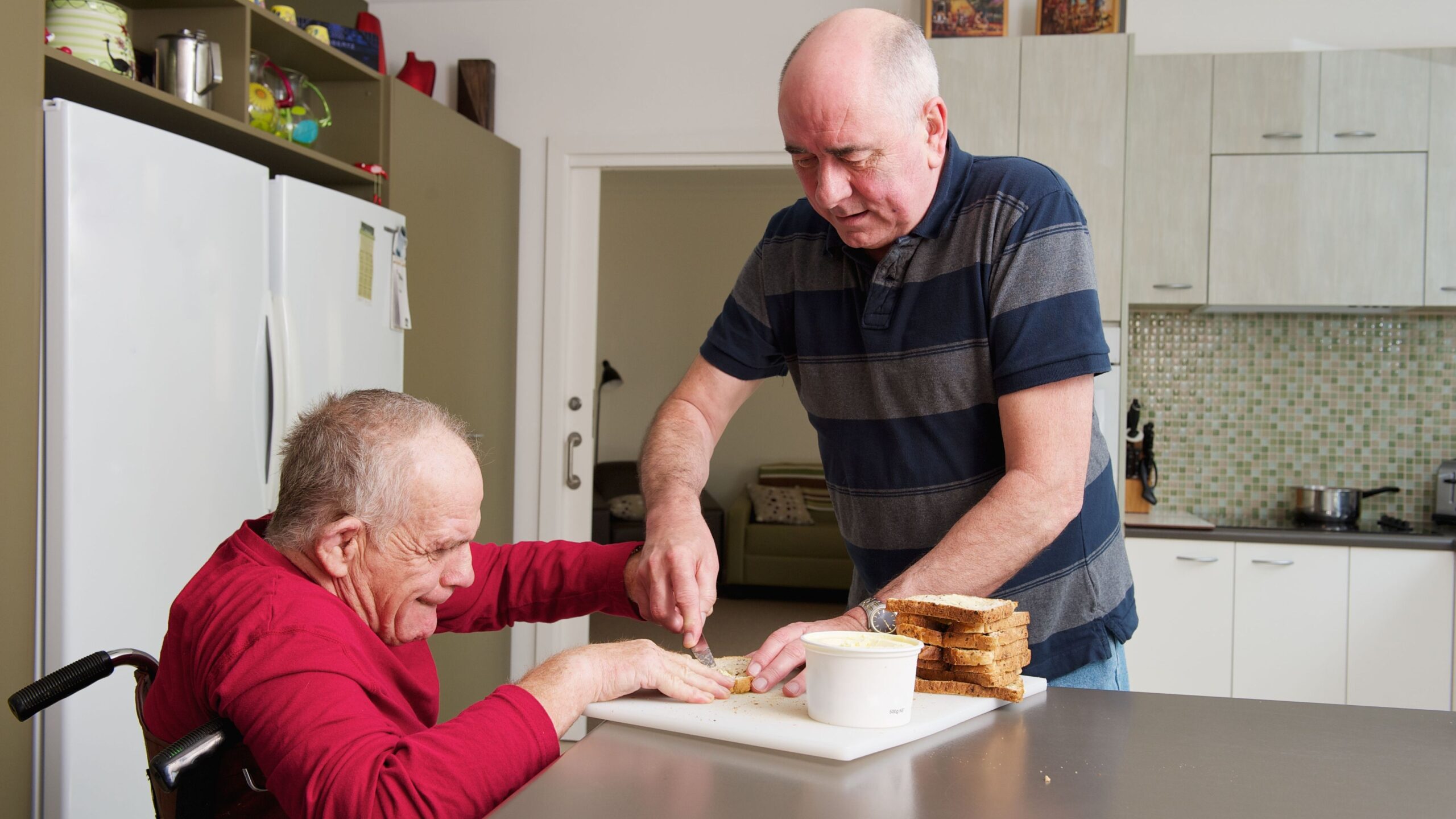 An aging adult in a wheelchair and his direct care professional prepare lunch in the kitchen